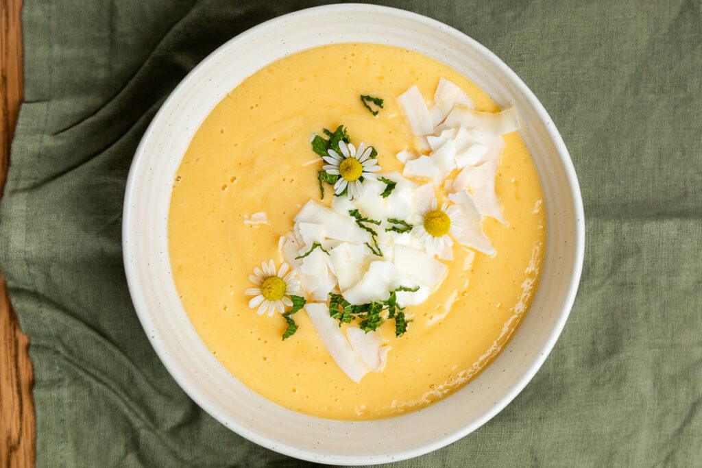 A bowl of mango smoothie on a green tablecloth.