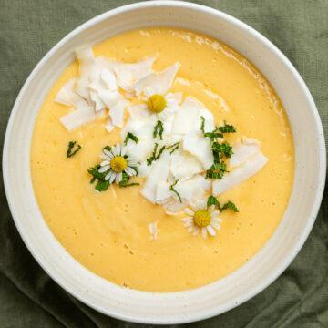 A mango smoothie bowl sprinkled with flaked coconut, chopped fresh mint and chamomile flowers.