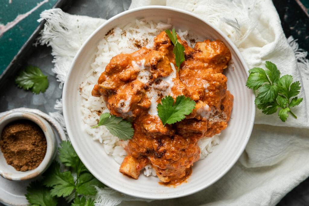 A bowl of butter chicken curry served with rice and fresh coriander.