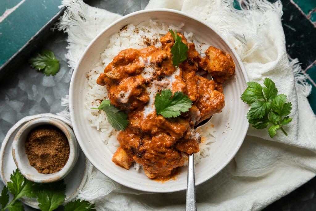 A bowl of butter chicken curry and rice with a spoon in it ready to eat.