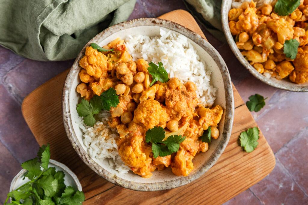 Two bowls of cauliflower and chickpea curry served with rice.