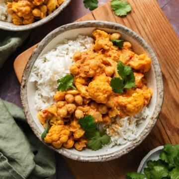 A bowl of cauliflower and chickpea curry served with rice and sprinkled with fresh coriandar.