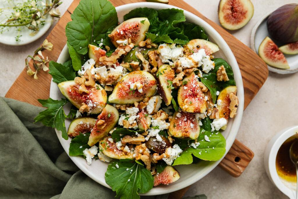 A serving bowl of fig and goats cheese salad on a wooden board.