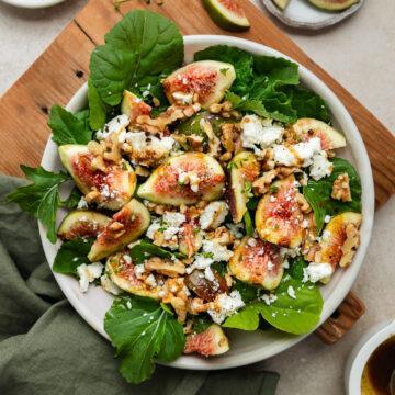 A bowl of fresh fig and goats cheese salad on a wooden board.