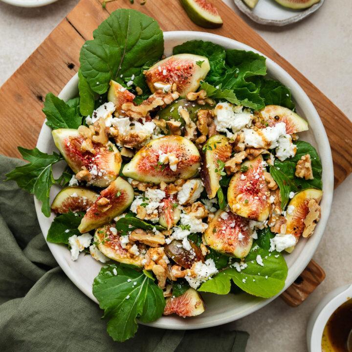 A bowl of fresh fig and goats cheese salad on a wooden board.