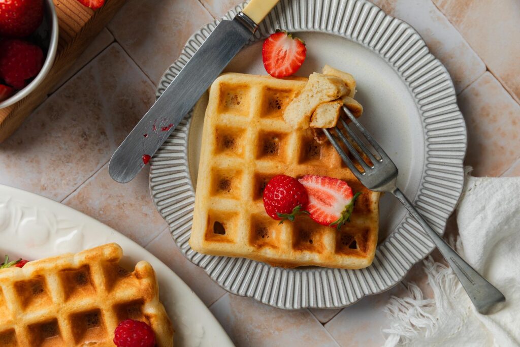 A waffle on a plate with a section taken out to show the fluffy texture.
