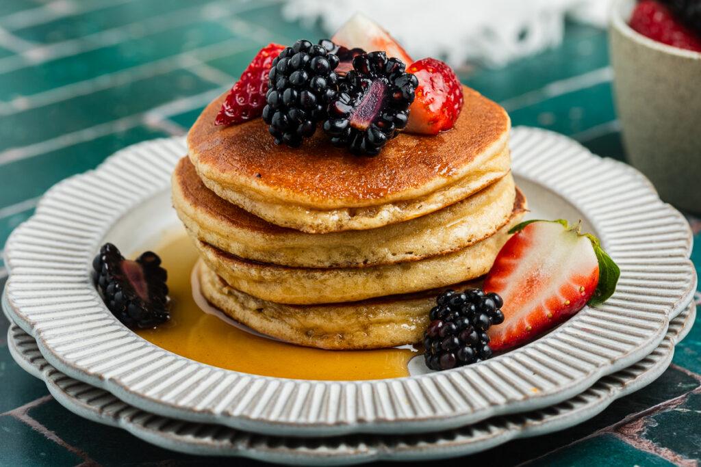 A stack of gluten-free almond meal pancakes served with fresh fruit and maple syrup.
