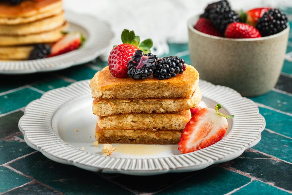 A stack of almond meal pancakes cut in half to show the fluffy texture, drizzled with maple syrup.