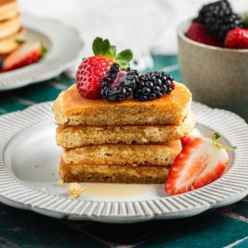 A cut stack of almond meal pancakes drizzled with maple syrup and served with fresh berries.
