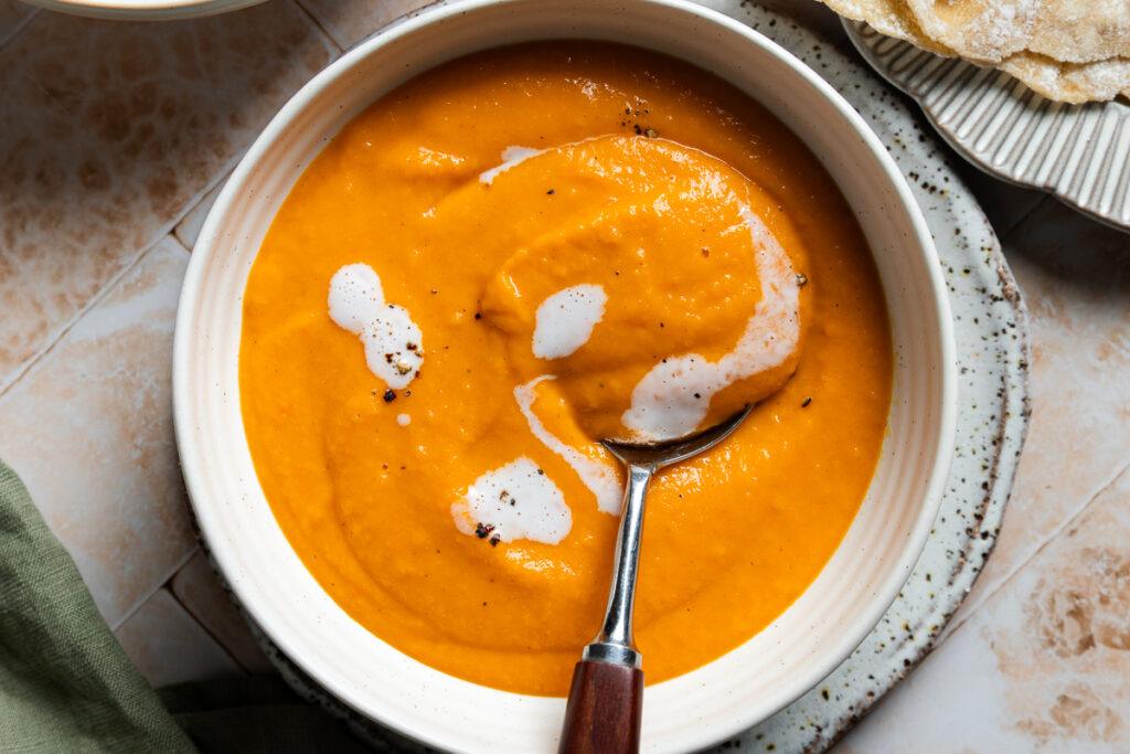 A bowl of gluten-free carrot and bean soup with a spoon in it.