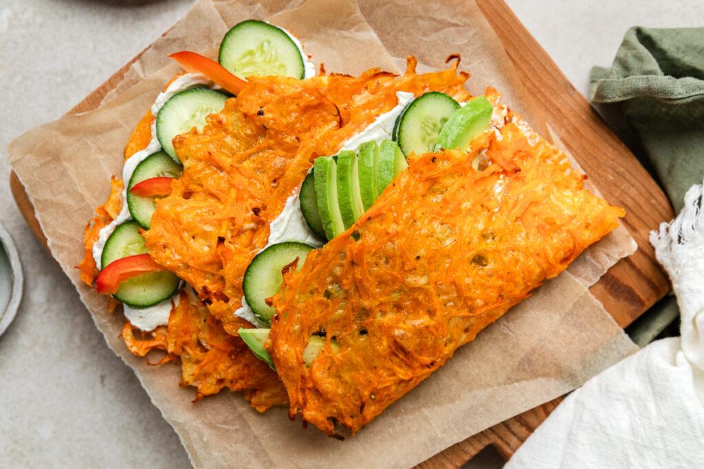Two carrot wraps filled with cucumber, avocado and cream cheese on a wooden board.