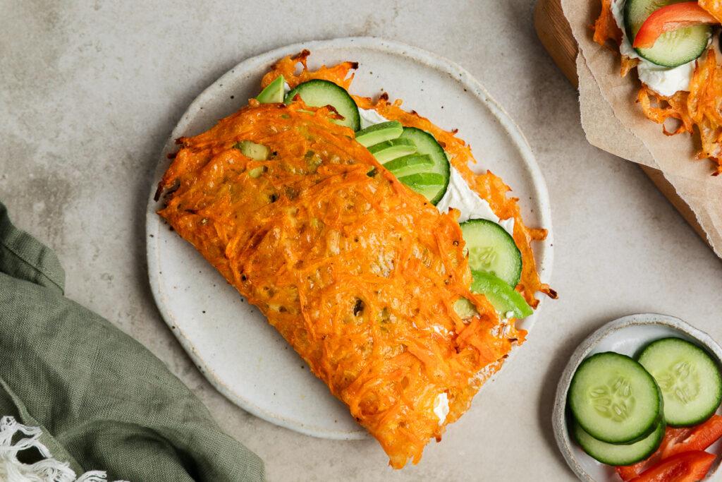 A carrot wrap on a plate filled with cream cheese and cucumber.