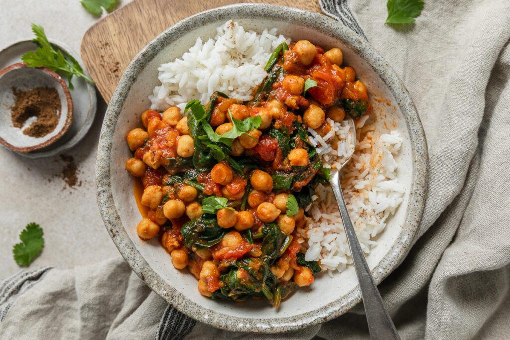 A bowl of chickpea and spinach curry served with rice, with a spoon in the bowl.