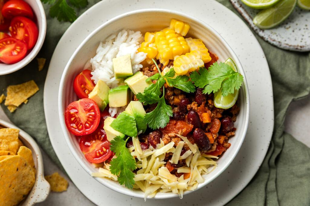 A chilli bowl topped with grated cheese, avocado and coriandar.