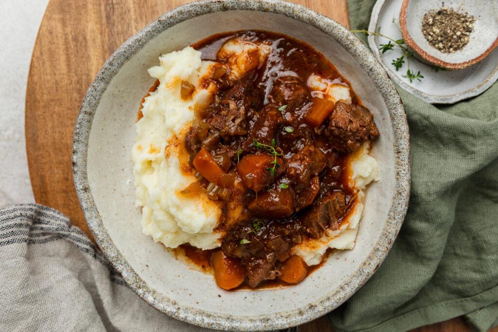 A bowl of slow cooker beef casserole served on mashed potato.