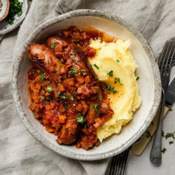 Slow cooker sausage casserole served with mashed potato.