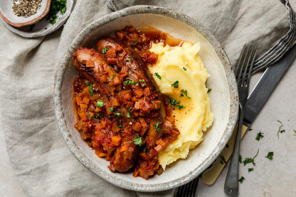 A bowl of slow cooker sausage casserole served with mashed potato.