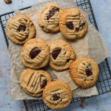 Baked almond meal choc chip cookies on baking paper on a wire cooling rack.