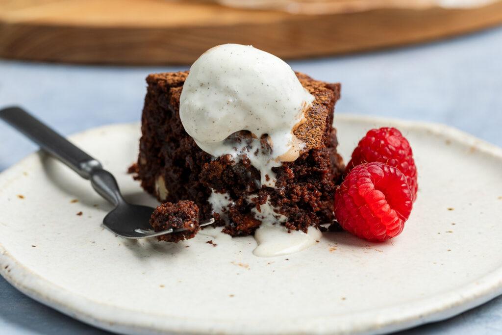 A slice of gluten-free brownie cake topped with a scoop of ice cream.