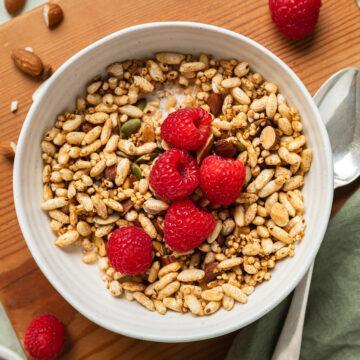 A bowl of gluten-free granola topped with fresh raspberries.