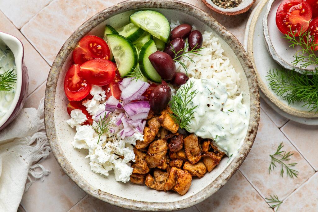 A Greek chicken bowl ready to eat, each ingredient put in the bowl separately.