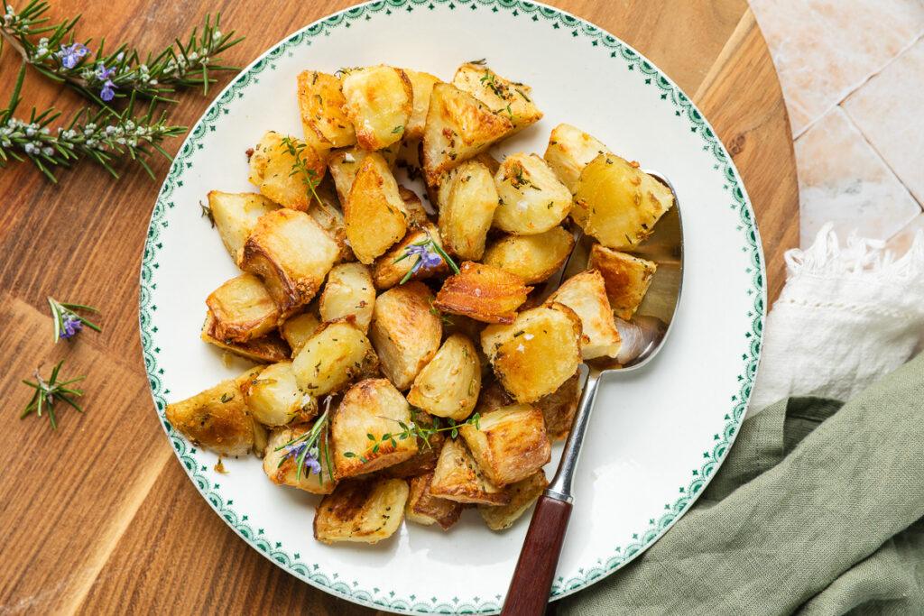 A plate of crunchy roast potatoes with a spoon ready to serve.