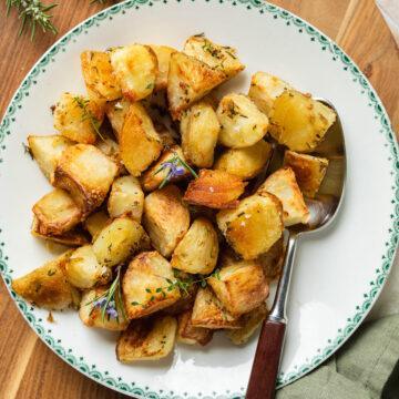 A bowl of crispy parmentier roast potatoes with a spoon ready to serve.