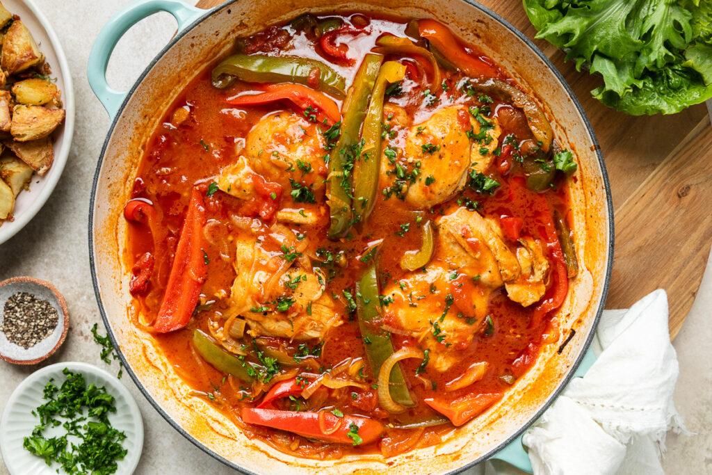 A pan of Basque chicken ready to serve, with salad and potatoes on the side.