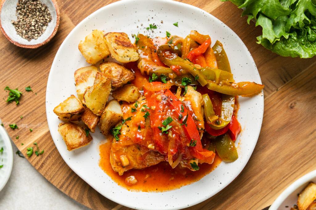 A plate of chicken and peppers served with roasted potatoes.