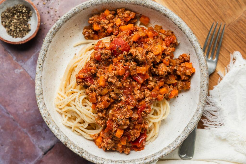A bowl of savoury mince spooned over gluten-free spaghetti to make a comforting kid-friendly dinner.