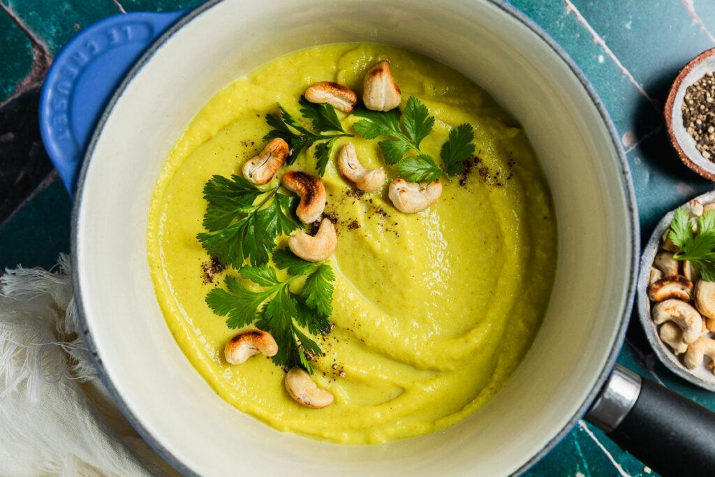 The homemade cauliflower soup in a saucepan topped with toasted cashew nuts.