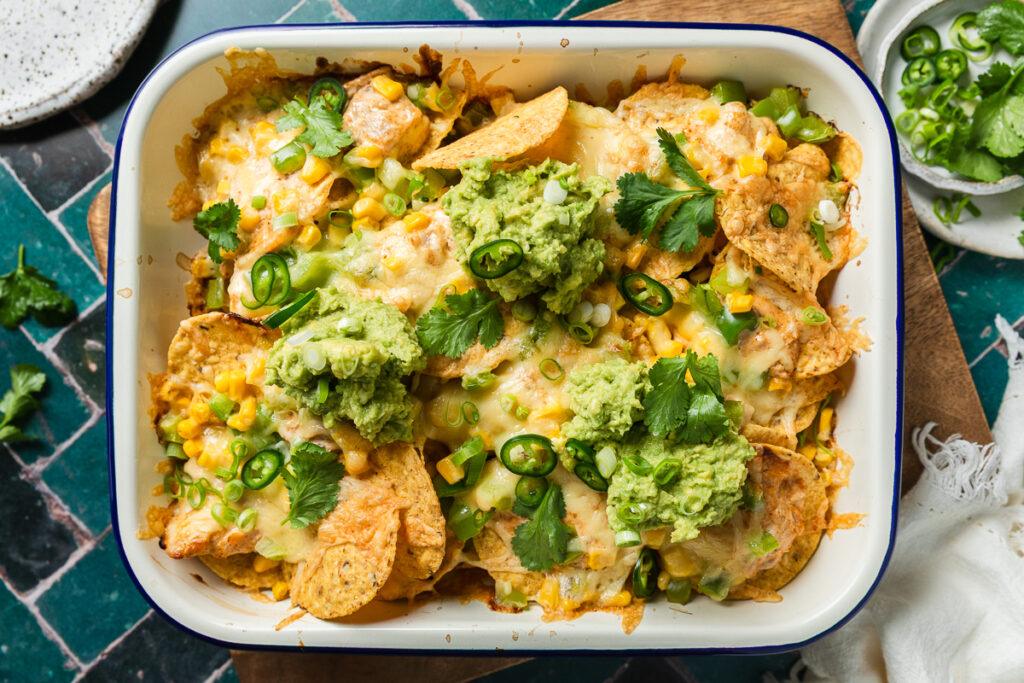 A baking dish of freshly baked tuna nachos topped with fresh coriander and avocado.