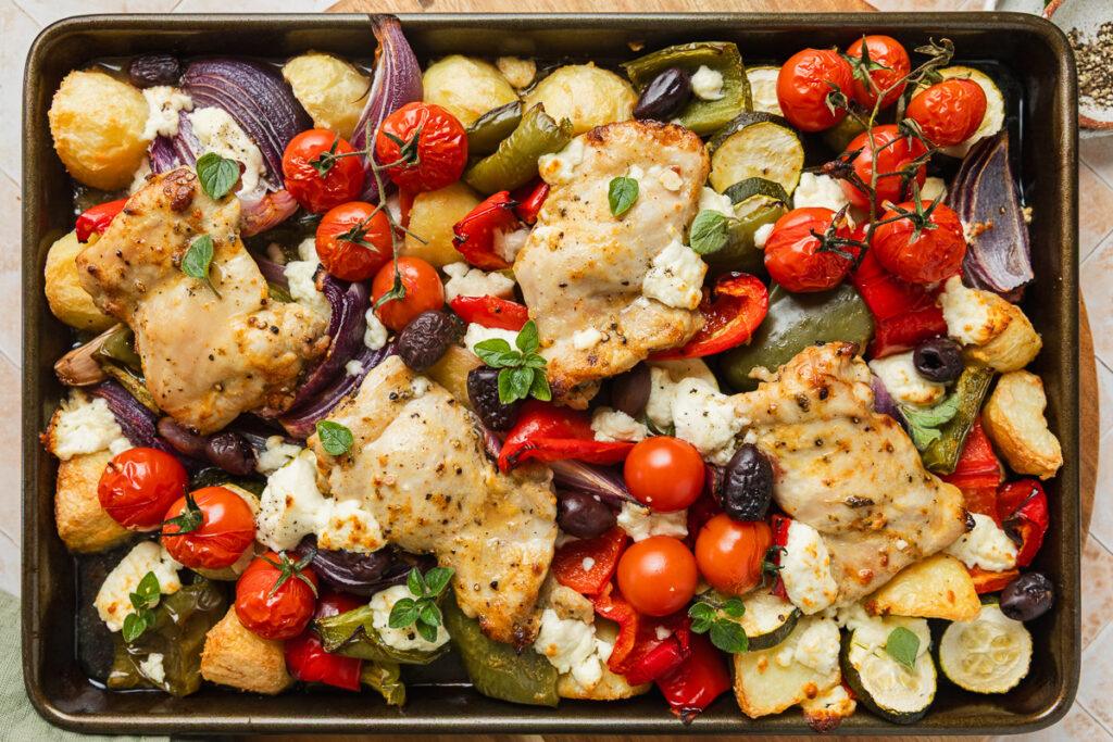 A tray of the chicken, vegetables and potatoes sprinkled with feta and herbs.