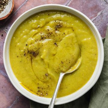 A bowl of dairy-free leek and potato soup with a spoon in it.