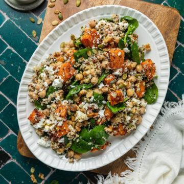 A serving plate of sweet potato and quinoa salad with pumpkin seeds scattered over the background.