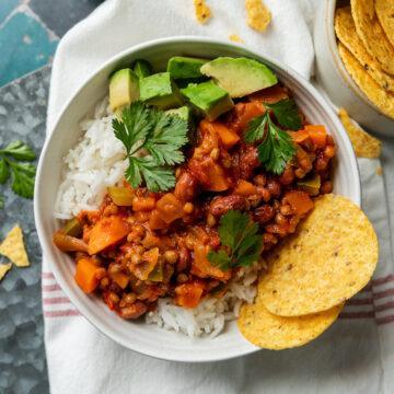 A bowl of homemade vegetarian chilli served with cubed avocado, corn chips and rice.