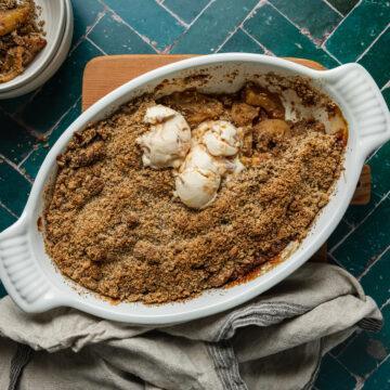 Homemade gluten-free apple crumble in a dish topped with scoops of ice cream.
